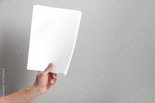 Man holding sheets of paper on grey background, closeup. Mockup for design