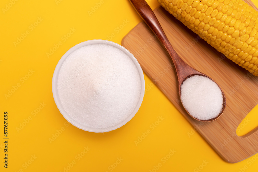 Natural sweetener Erythritol, produced by fermentation from corn in ceramic bowl, wooden spoon, corncob on yellow orange background. Sugar substitute. Horizontal plane, top view. Natural sweetener Erythritol, produced by fermentation from corn in ceramic bowl, wooden spoon, corncob on yellow orange background. Sugar substitute. Horizontal plane, top view.