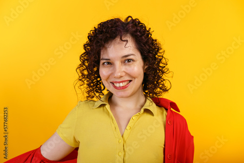 Studio shot of positive and smiling pretty female. Curly laughing girl in bright yellow shirt. Isolated on yellow background. Close up. Copy space.