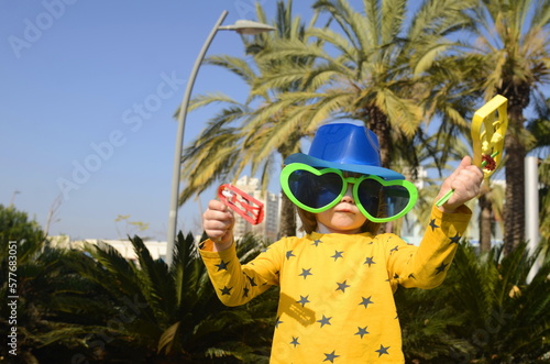 Carnival, Purim in Israel. A cheerful little boy in a hat, funny glasses, a wig with a rattle, Raashan. Portrait of a child in a costume of Klana, a funny holiday, a birthday, a masquerade. photo