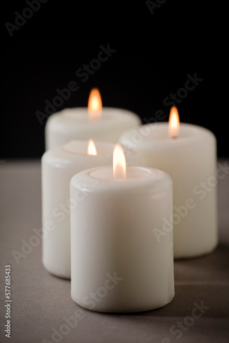 set of burning white candles on the shelf with black background