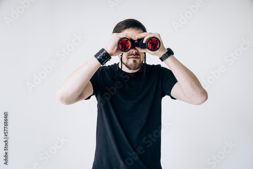 A guy in a black t-shirt holds binoculars and looks into it