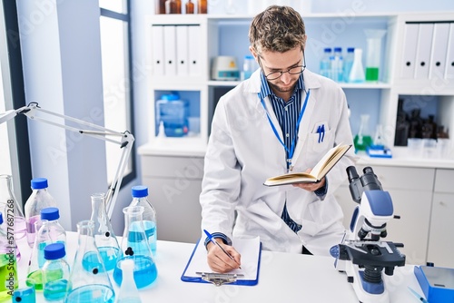 Young man scientist writing report reading book at laboratory