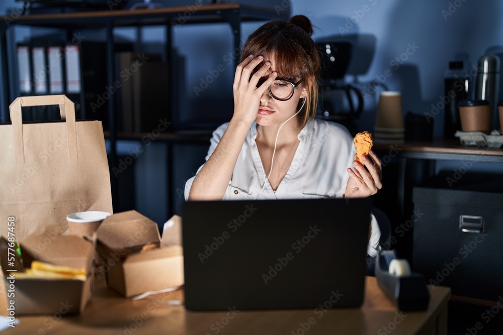 Young beautiful woman working using computer laptop and eating delivery food yawning tired covering half face, eye and mouth with hand. face hurts in pain. Young beautiful woman working using computer laptop and eating delivery food yawning tired covering half face, eye and mouth with hand. face hurts in pain.