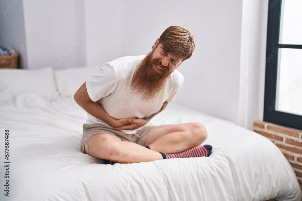 Young redhead man suffering for stomach ache sitting on bed at bedroom Young redhead man suffering for stomach ache sitting on bed at bedroom