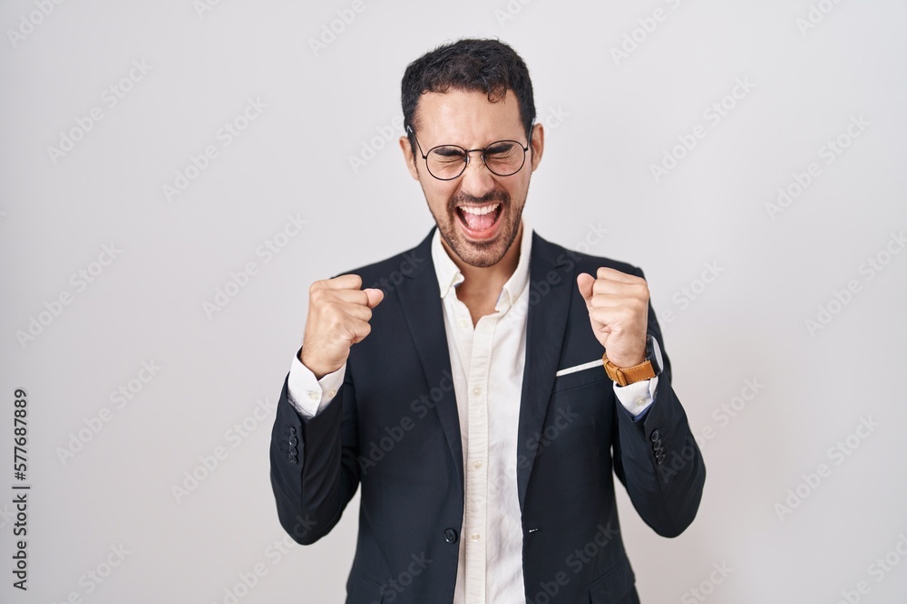 Handsome business hispanic man standing over white background excited for success with arms raised and eyes closed celebrating victory smiling. winner concept. Handsome business hispanic man standing over white background excited for success with arms raised and eyes closed celebrating victory smiling. winner concept.