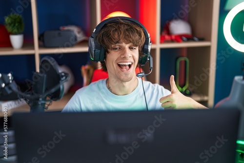 Hispanic young man playing video games smiling happy and positive, thumb up doing excellent and approval sign