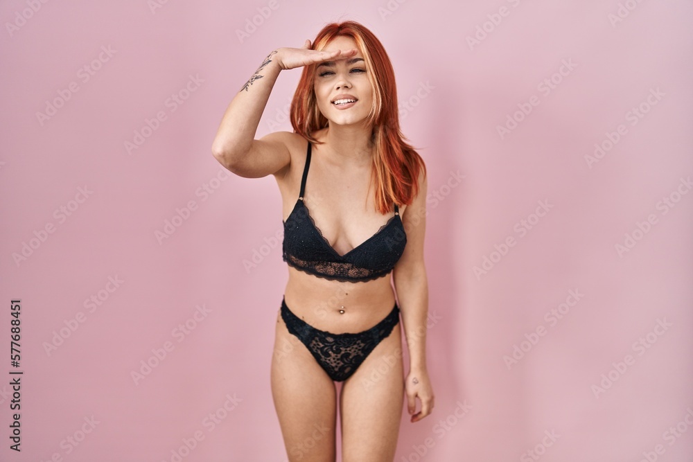Obraz premium Young caucasian woman wearing lingerie over pink background very happy and smiling looking far away with hand over head. searching concept.