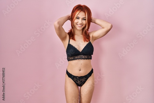 Young caucasian woman wearing lingerie over pink background relaxing and stretching, arms and hands behind head and neck smiling happy