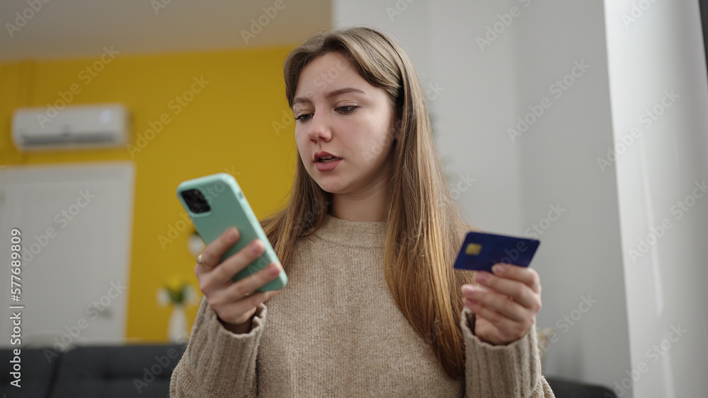 Young blonde woman using smartphone and credit card sitting on floor at home Young blonde woman using smartphone and credit card sitting on floor at home
