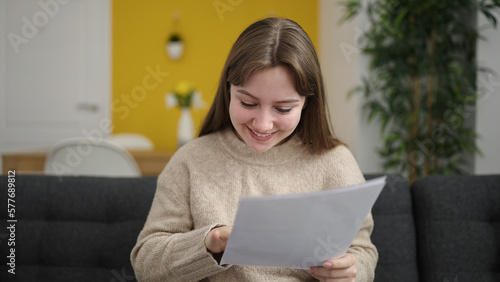 Young blonde woman reading document sitting on sofa at home