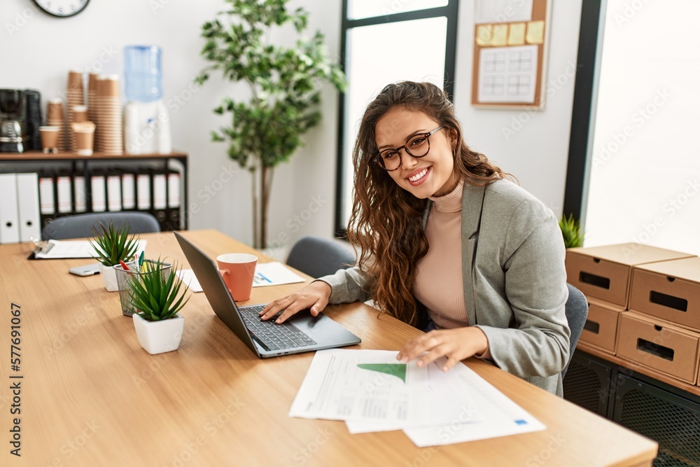Young beautiful hispanic woman business worker using laptop reading document at office Young beautiful hispanic woman business worker using laptop reading document at office