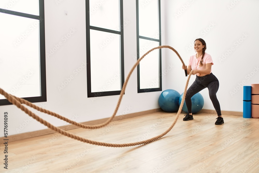 Young beautiful hispanic woman smiling confident using battle rope training at sport center