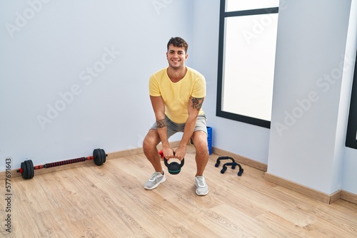 Young hispanic man smiling confident using kettlebell training at sport center
