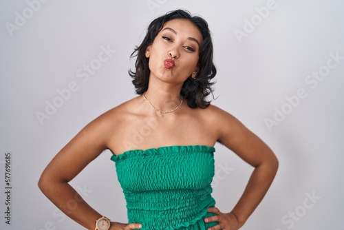 Young hispanic woman standing over isolated background looking at the camera blowing a kiss on air being lovely and sexy. love expression.