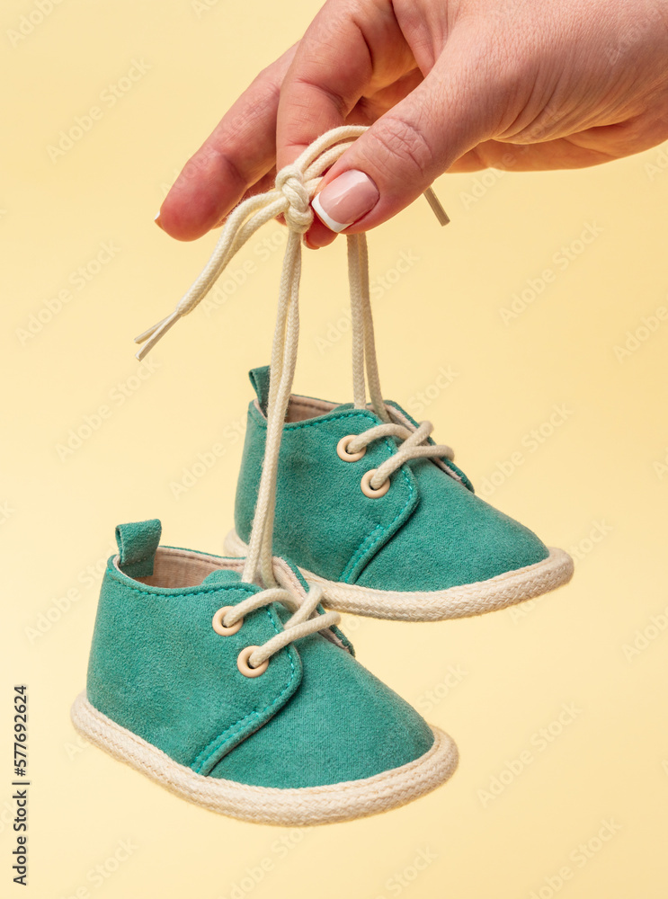 Female hand holding newborn baby shoes with laces