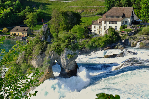 Rocky cliffs stand by the water force of Rhine waterfalls in Neuhausen, Schaffausen, Switzerland. Daylight photography of the largest waterfalls in Europe, green vegetation in Spring photo