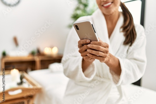 Young latin woman wearing bathrobe using smartphone