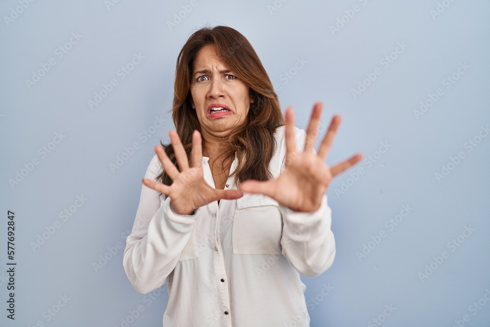 Hispanic woman standing over isolated background afraid and terrified with fear expression stop gesture with hands, shouting in shock. panic concept. Hispanic woman standing over isolated background afraid and terrified with fear expression stop gesture with hands, shouting in shock. panic concept.