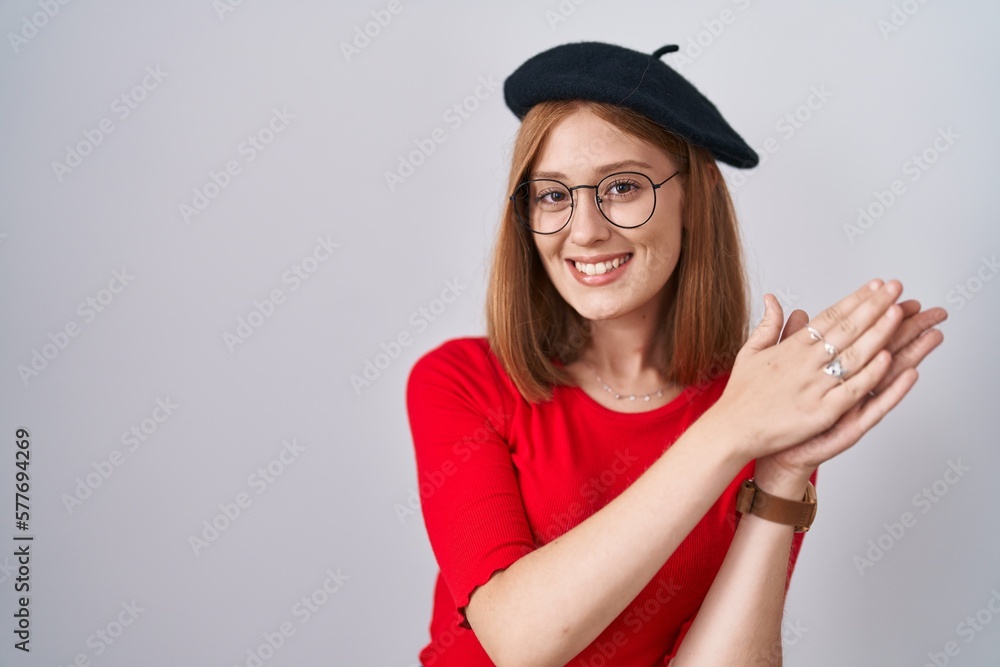 Young redhead woman standing wearing glasses and beret clapping and applauding happy and joyful, smiling proud hands together Young redhead woman standing wearing glasses and beret clapping and applauding happy and joyful, smiling proud hands together