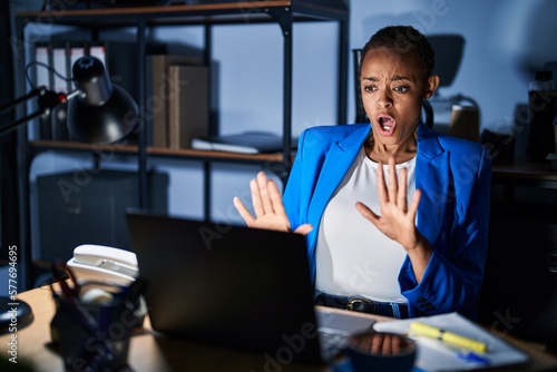 Beautiful african american woman working at the office at night afraid and terrified with fear expression stop gesture with hands  shouting in shock. panic concept.