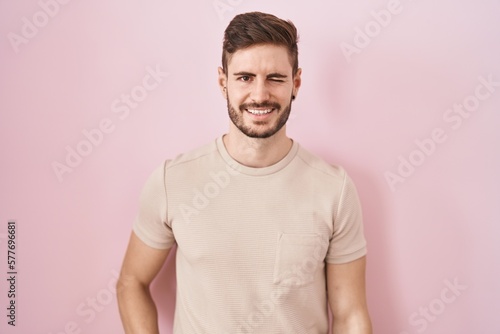 Hispanic man with beard standing over pink background winking looking at the camera with sexy expression, cheerful and happy face. © Krakenimages.com