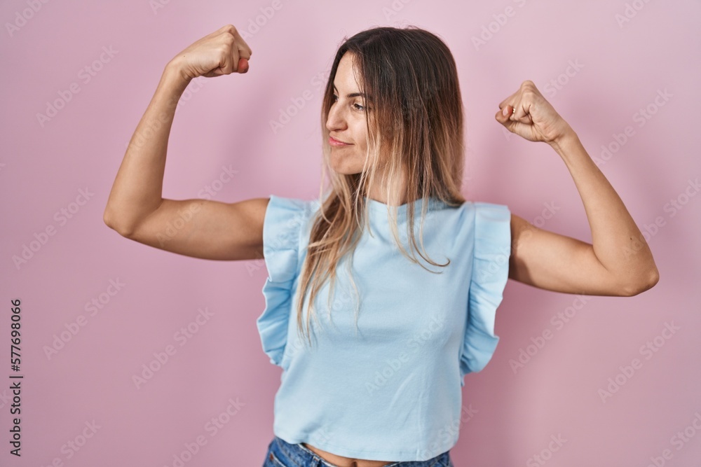 Young hispanic woman standing over pink background showing arms muscles smiling proud. fitness concept. Young hispanic woman standing over pink background showing arms muscles smiling proud. fitness concept.