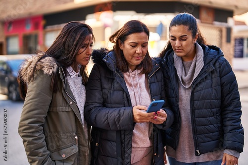 Three woman mother and daughters using smartphone at street