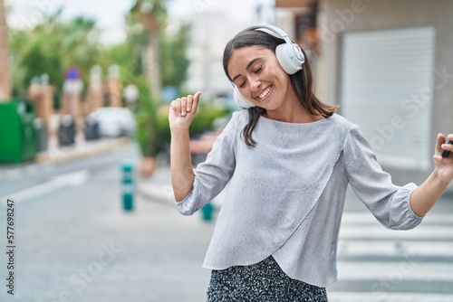 Young beautiful hispanic woman listening to music and dancing at street