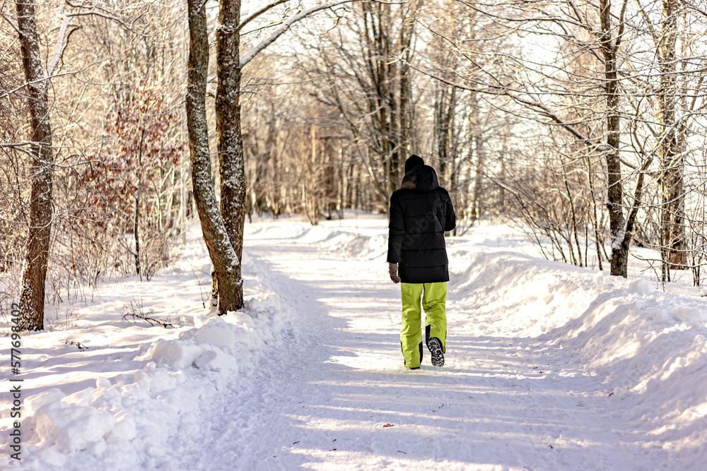 A man in a dark jacket and yellow sweatpants walks in a winter park