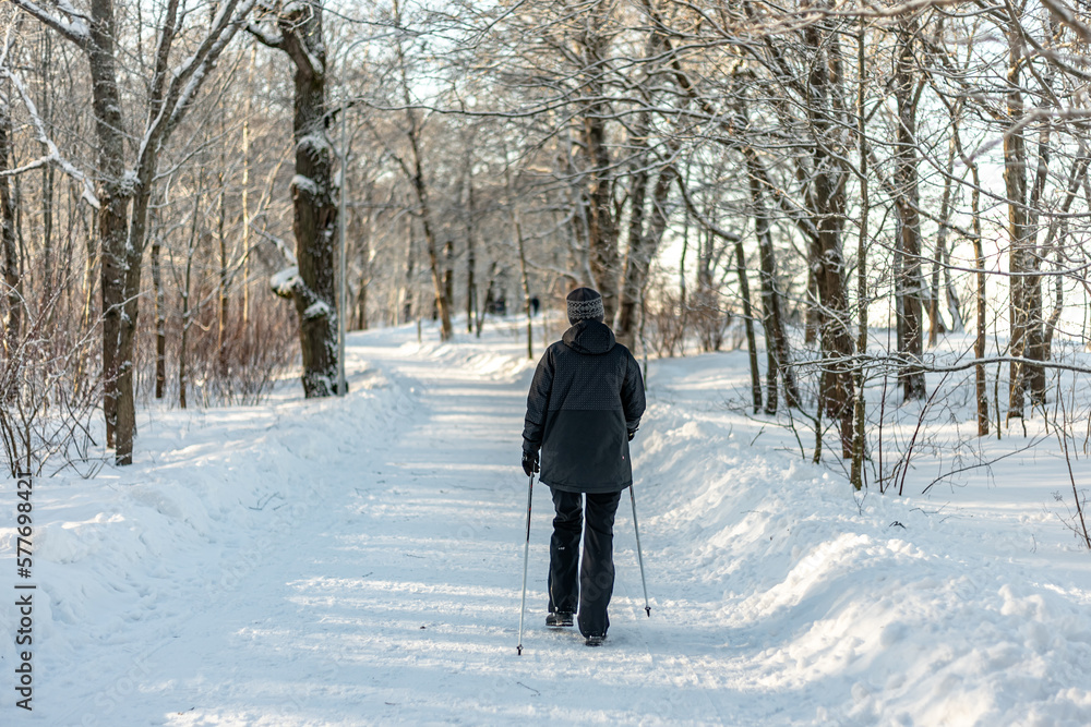A woman in a dark jacket walks in a winter park with Scandinavian sticks