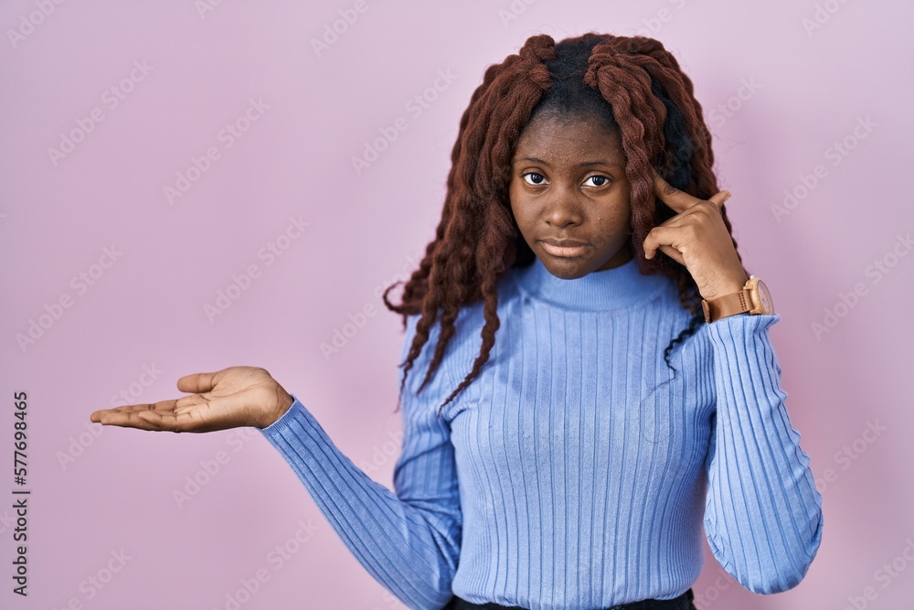 African woman standing over pink background confused and annoyed with open palm showing copy space and pointing finger to forehead. think about it. African woman standing over pink background confused and annoyed with open palm showing copy space and pointing finger to forehead. think about it.