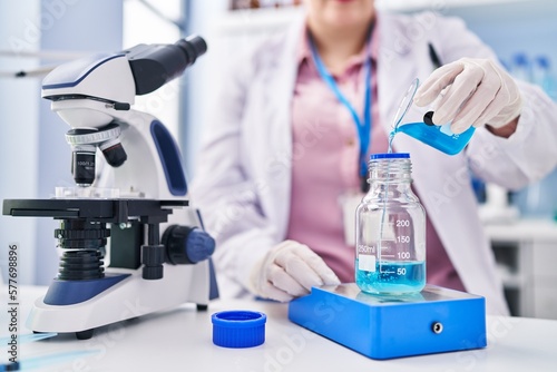 Young beautiful plus size woman scientist pouring liquid on test tube weighing liquid at laboratory