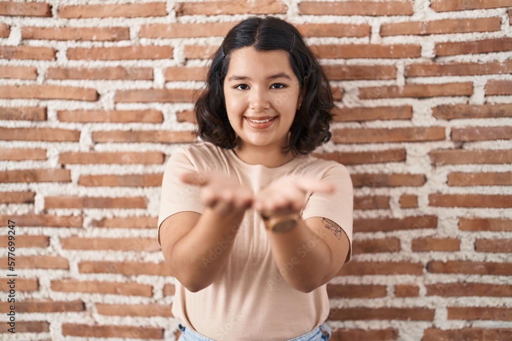 Young hispanic woman standing over bricks wall smiling with hands palms together receiving or giving gesture. hold and protection Young hispanic woman standing over bricks wall smiling with hands palms together receiving or giving gesture. hold and protection