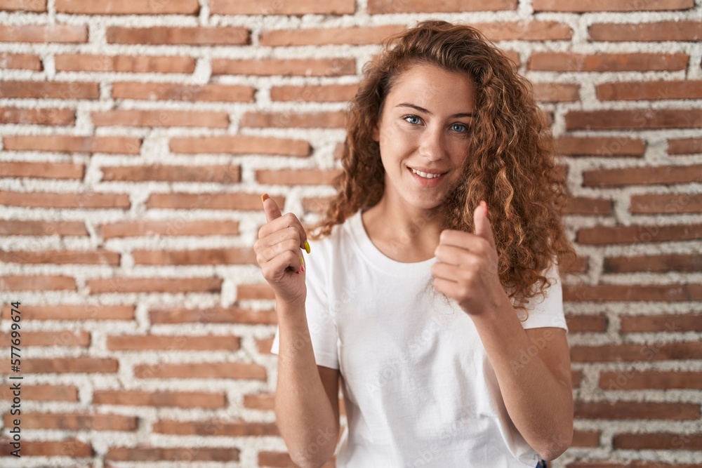 Young caucasian woman standing over bricks wall background success sign doing positive gesture with hand, thumbs up smiling and happy. cheerful expression and winner gesture. Young caucasian woman standing over bricks wall background success sign doing positive gesture with hand, thumbs up smiling and happy. cheerful expression and winner gesture.