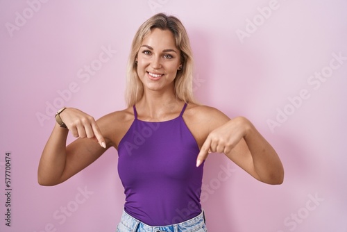 Young blonde woman standing over pink background looking confident with smile on face, pointing oneself with fingers proud and happy. © Krakenimages.com