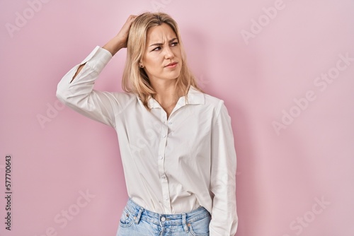 Young caucasian woman wearing casual white shirt over pink background confuse and wondering about question. uncertain with doubt, thinking with hand on head. pensive concept. © Krakenimages.com