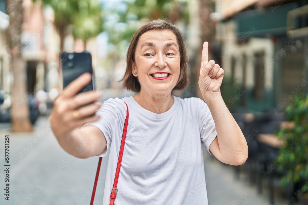 Middle age hispanic woman doing video call with smartphone smiling with an idea or question pointing finger with happy face, number one Middle age hispanic woman doing video call with smartphone smiling with an idea or question pointing finger with happy face, number one