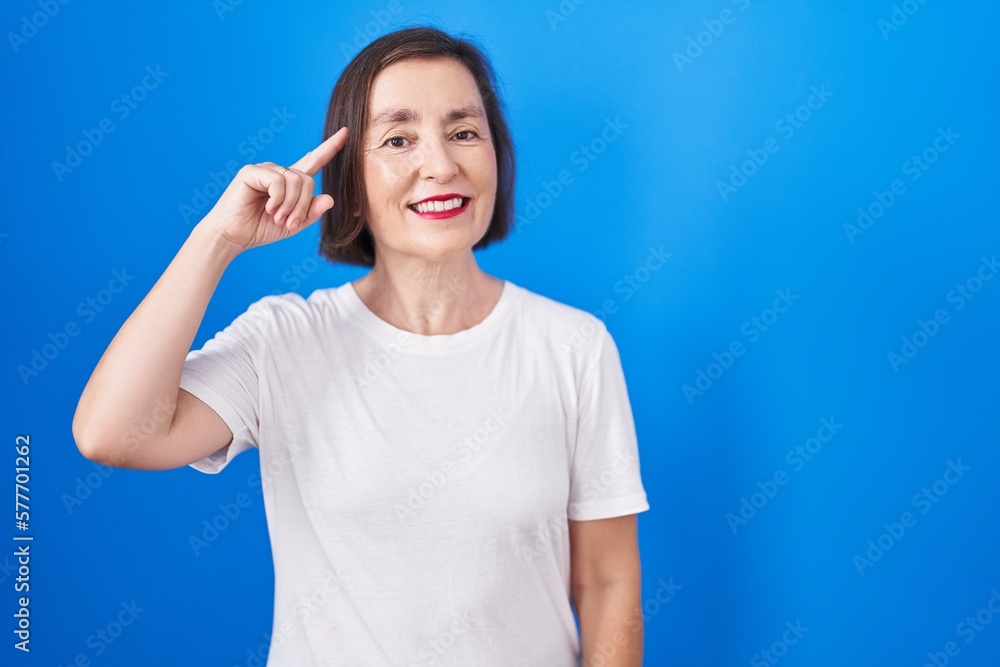Middle age hispanic woman standing over blue background smiling pointing to head with one finger, great idea or thought, good memory Middle age hispanic woman standing over blue background smiling pointing to head with one finger, great idea or thought, good memory