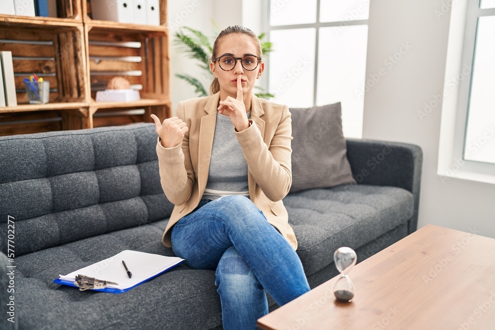 Young woman working at consultation office asking to be quiet with finger on lips pointing with hand to the side. silence and secret concept. Young woman working at consultation office asking to be quiet with finger on lips pointing with hand to the side. silence and secret concept.