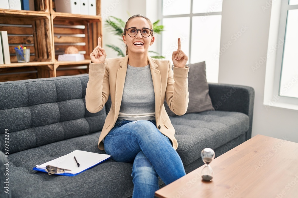 Young woman working at consultation office smiling amazed and surprised and pointing up with fingers and raised arms. Young woman working at consultation office smiling amazed and surprised and pointing up with fingers and raised arms.