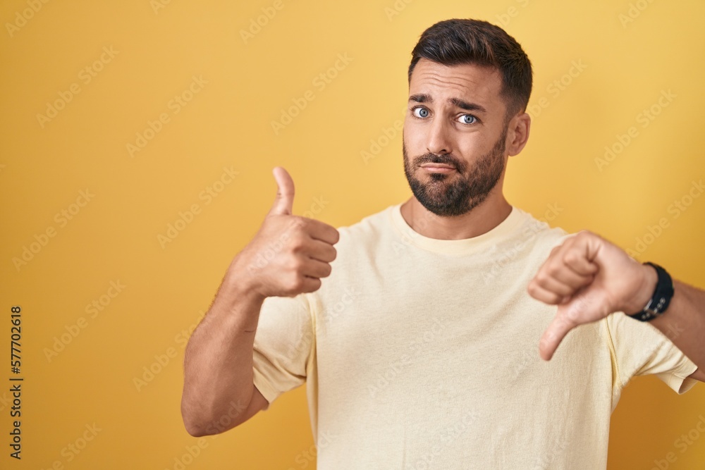 Handsome hispanic man standing over yellow background doing thumbs up and down, disagreement and agreement expression. crazy conflict Handsome hispanic man standing over yellow background doing thumbs up and down, disagreement and agreement expression. crazy conflict