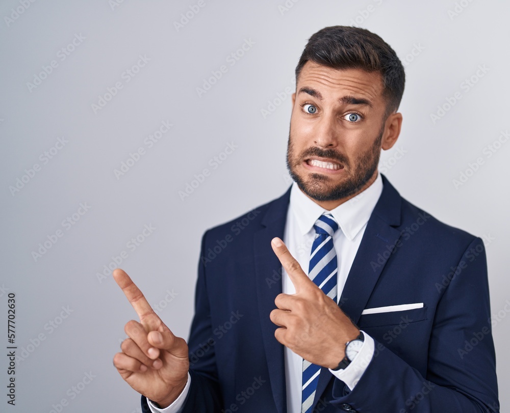 Handsome hispanic man wearing suit and tie pointing aside worried and nervous with both hands, concerned and surprised expression Handsome hispanic man wearing suit and tie pointing aside worried and nervous with both hands, concerned and surprised expression