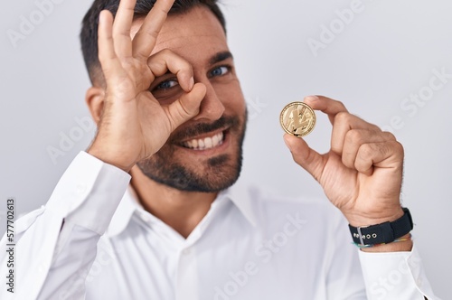 Handsome hispanic man holding litecoin cryptocurrency coin smiling happy doing ok sign with hand on eye looking through fingers