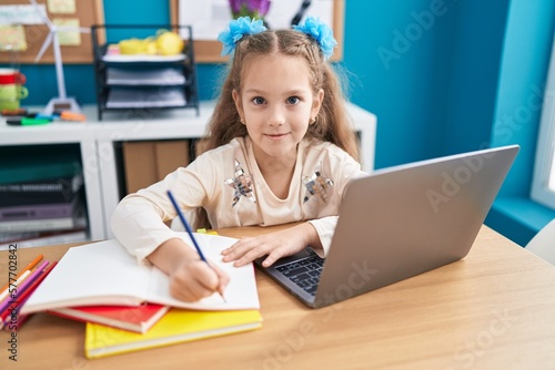 Adorable caucasian girl student using laptop writing on notebook at office