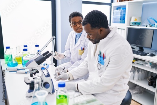 Man and woman scientists writing on notebook working at laboratory