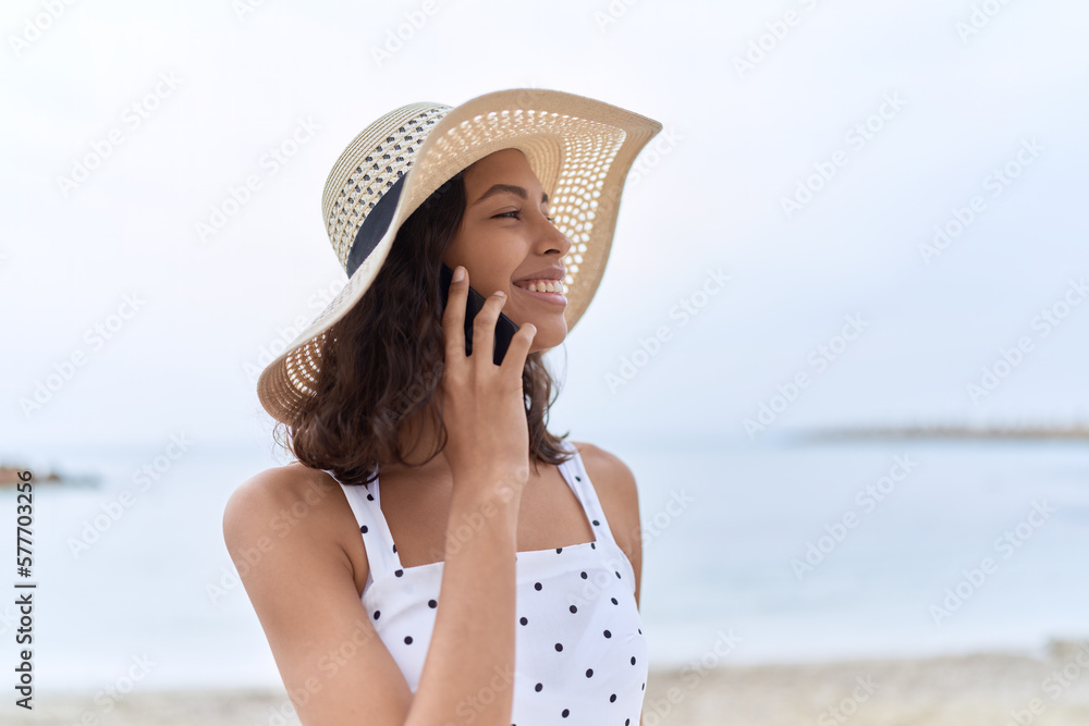 Young african american woman wearing summer hat talking on smartphone at seaside