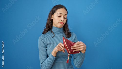 Young beautiful hispanic woman showing empty wallet over isolated blue background