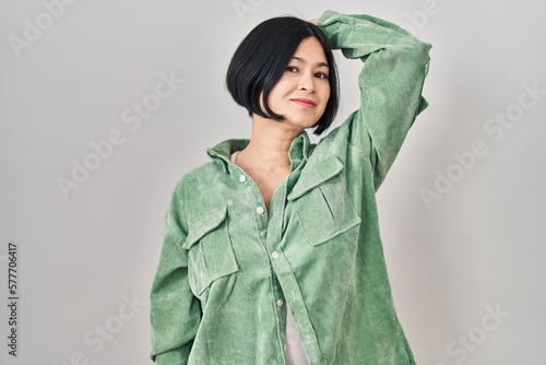 Young asian woman standing over white background smiling confident touching hair with hand up gesture, posing attractive and fashionable