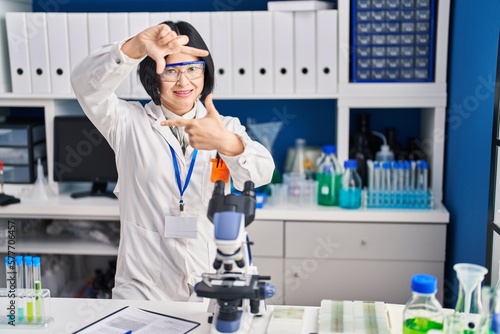 Young asian woman working at scientist laboratory smiling making frame with hands and fingers with happy face. creativity and photography concept.